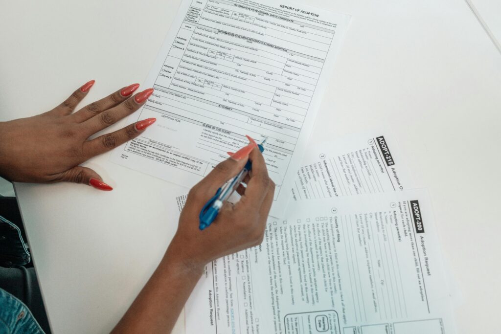 A woman with red nails fills out adoption application forms on a desk.