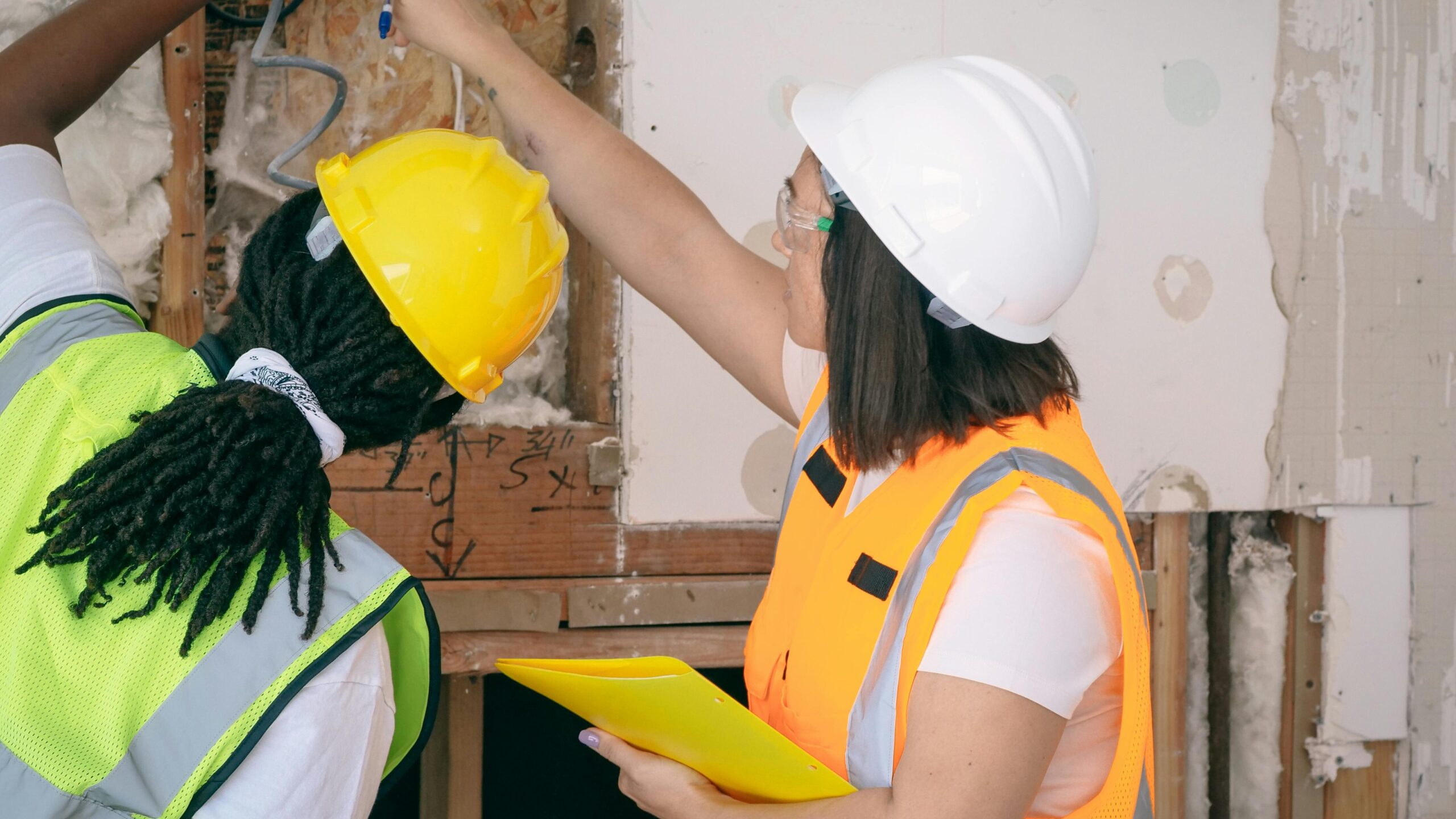 Two female engineers in safety gear inspecting wiring. Professional, safe, and collaborative workplace environment.